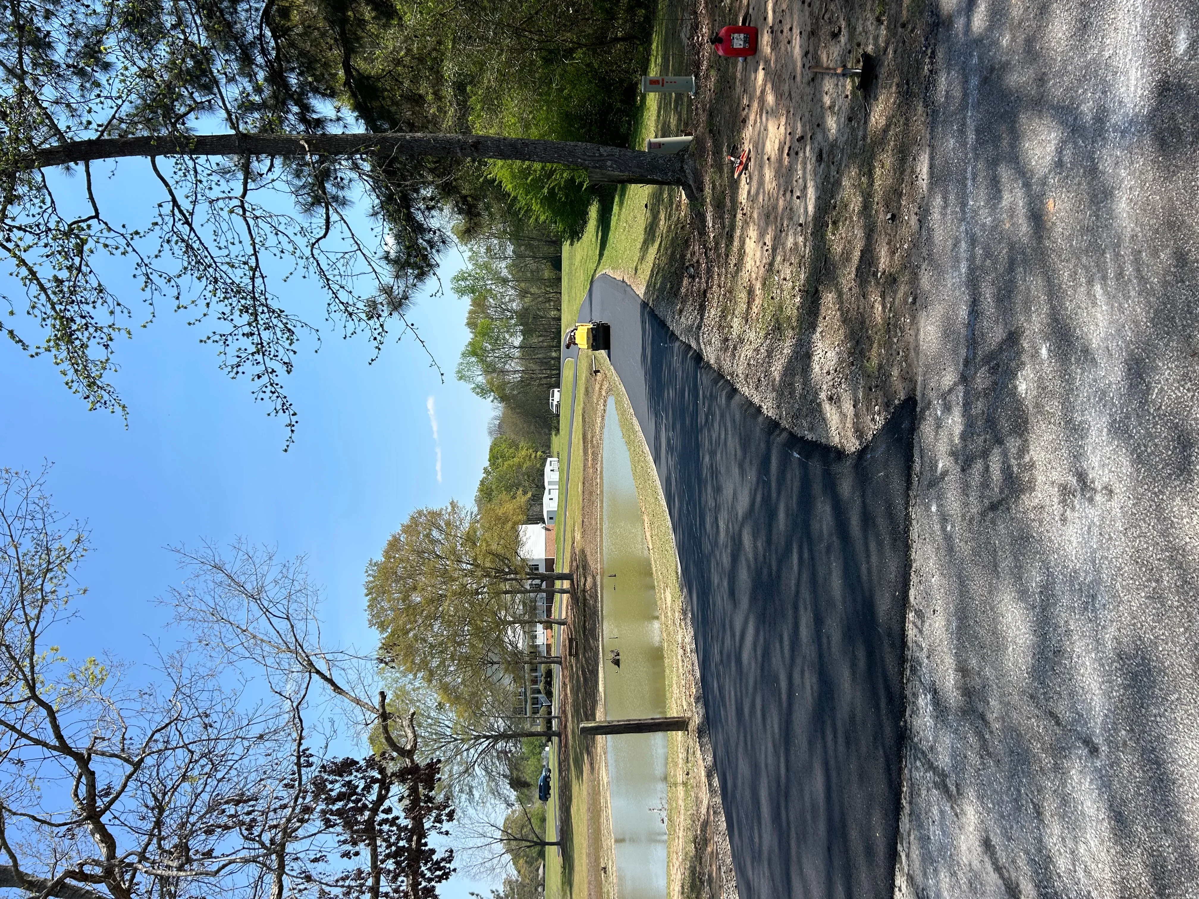 Residential driveway with fresh asphalt overlay and cleared surface, bordered by grass and stone foundation