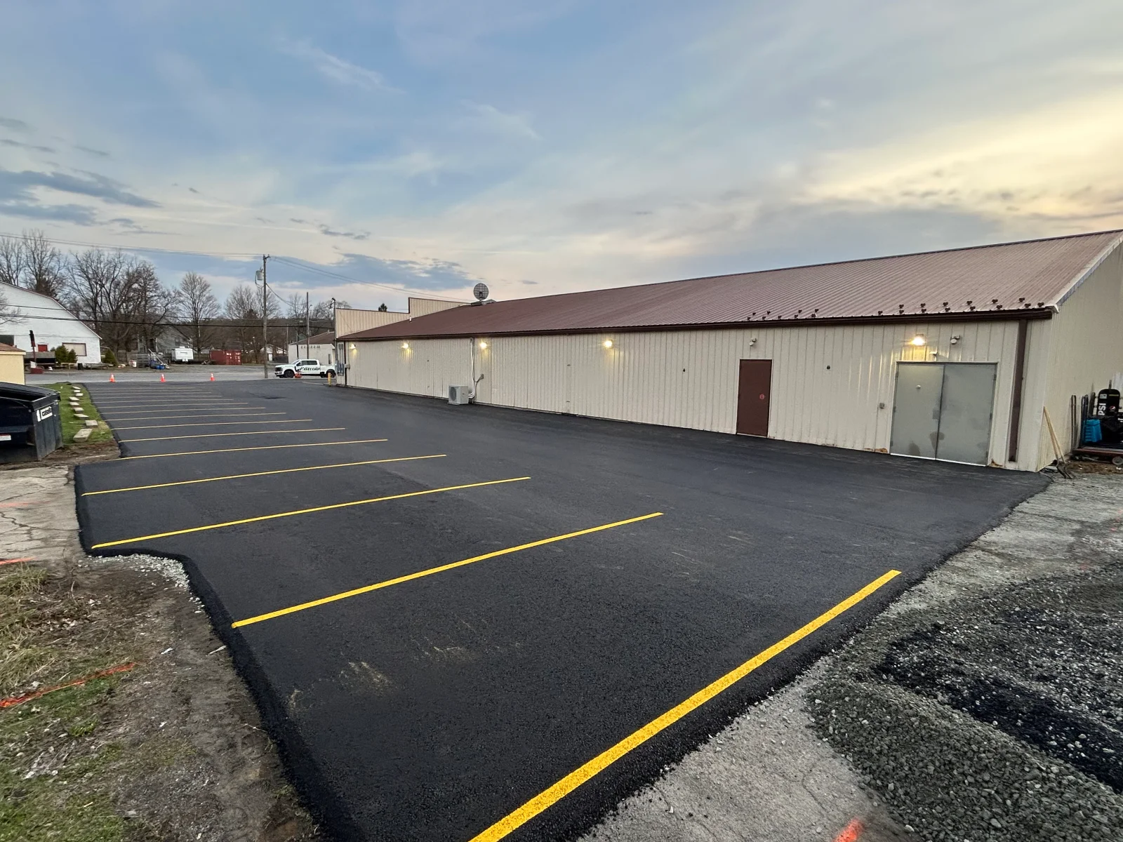 New asphalt parking lot with yellow line striping and metal building backdrop