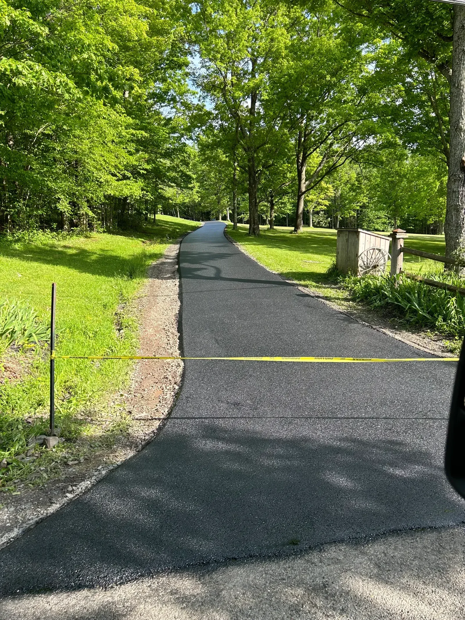 Fresh asphalt driveway with clean edges and yellow line marking, bordered by green lawn