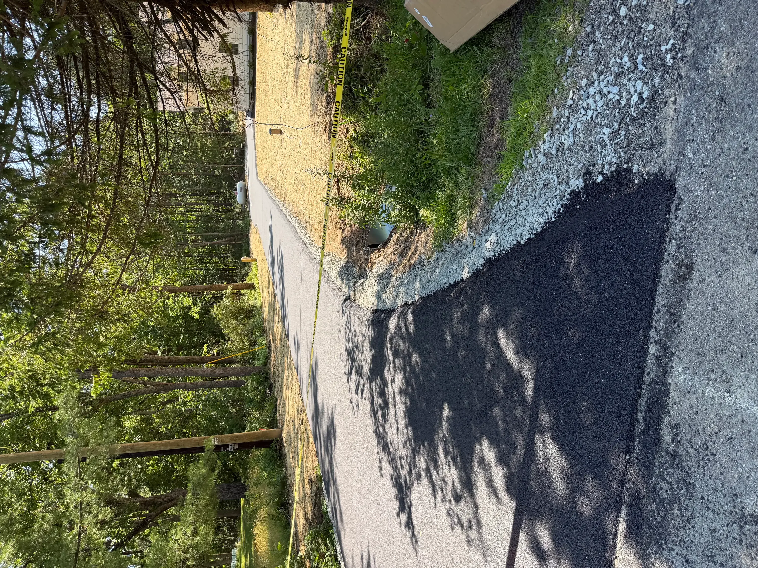 Newly paved black asphalt driveway with concrete edging and graded shoulders