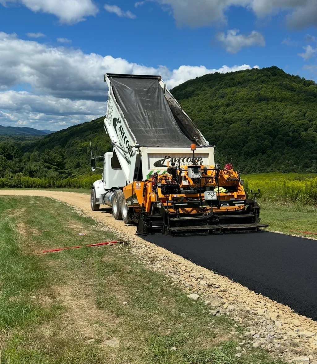 Asphalt paver laying fresh black asphalt on prepared gravel base with dump truck